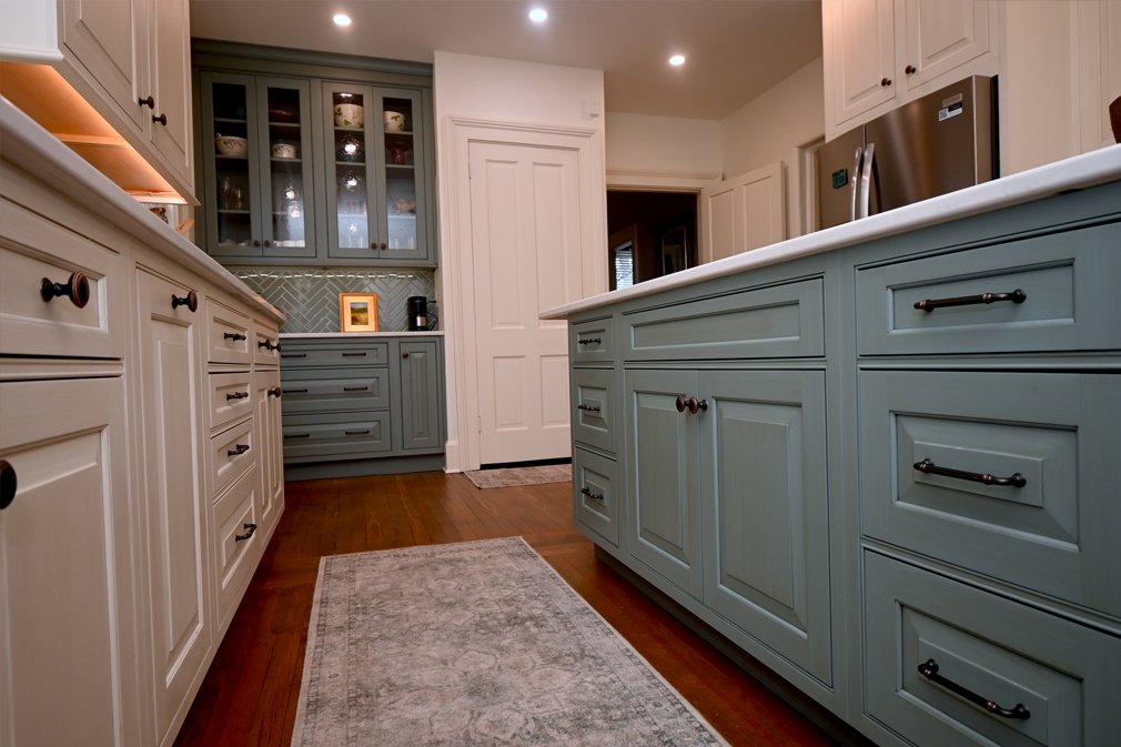 Kitchen with white and blue-green cabinets, a central island, and a patterned rug on a wood floor.