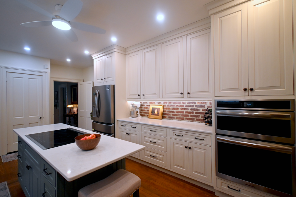 White kitchen with island, stainless steel appliances, brick backsplash.