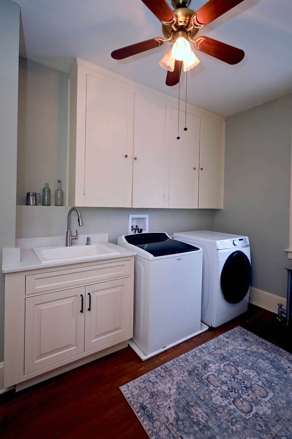 Laundry room with white cabinets, sink, washer, dryer, rug, and ceiling fan.