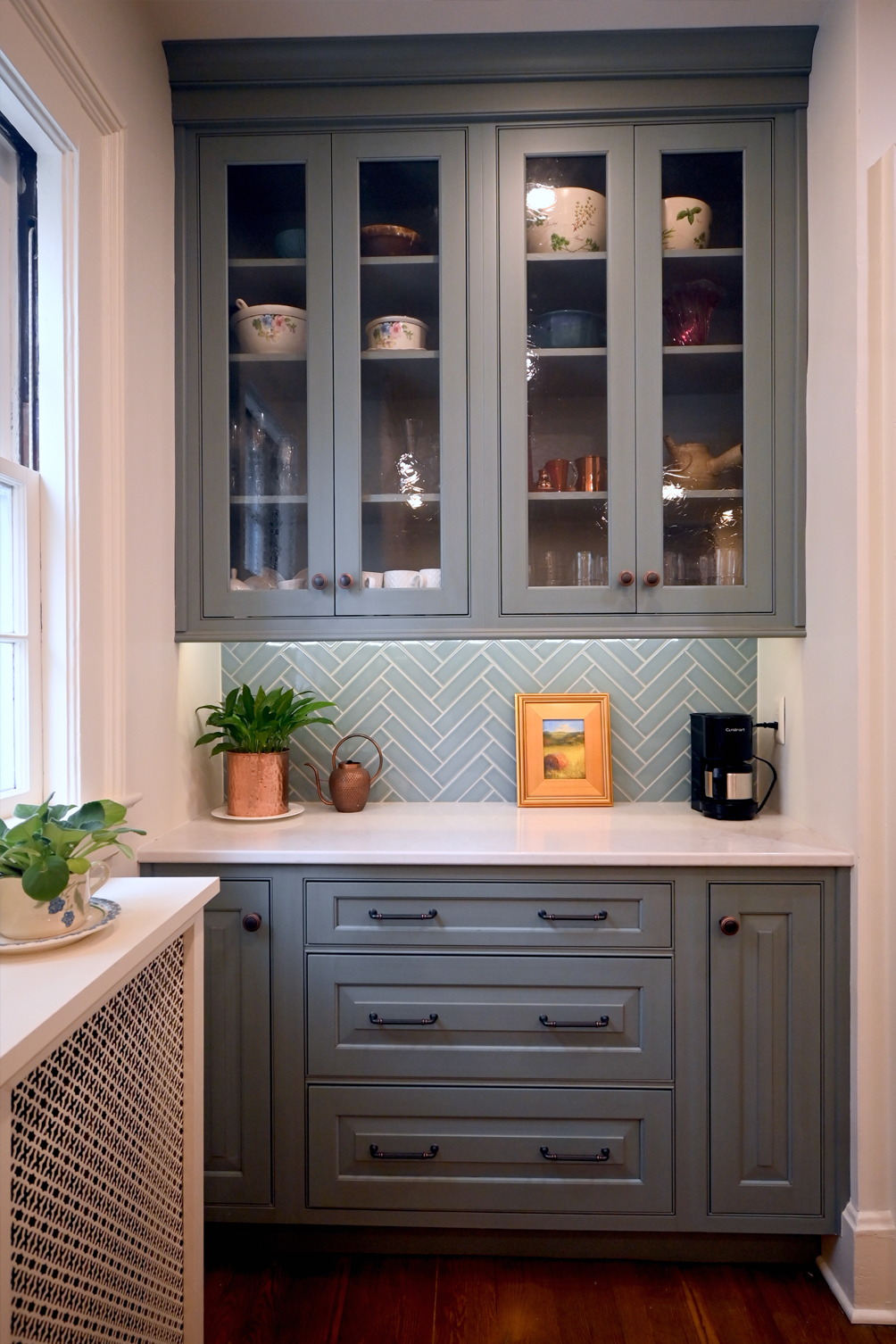 Blue-painted kitchen cabinets with glass doors, herringbone tile backsplash, and a coffee maker.