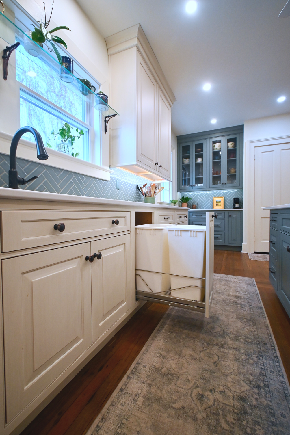 Kitchen with pull-out trash bins, white cabinets, and blue backsplash.
