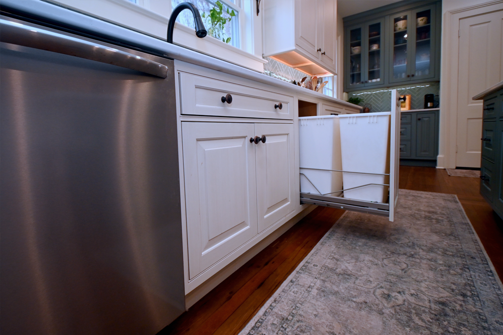 White kitchen cabinet with pull-out trash bins, stainless steel dishwasher.