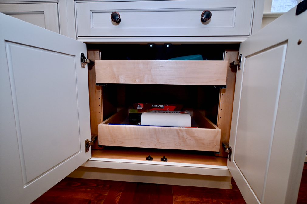 Cabinet with two pull-out drawers, open. Light wood drawers inside a white cabinet, some items visible.