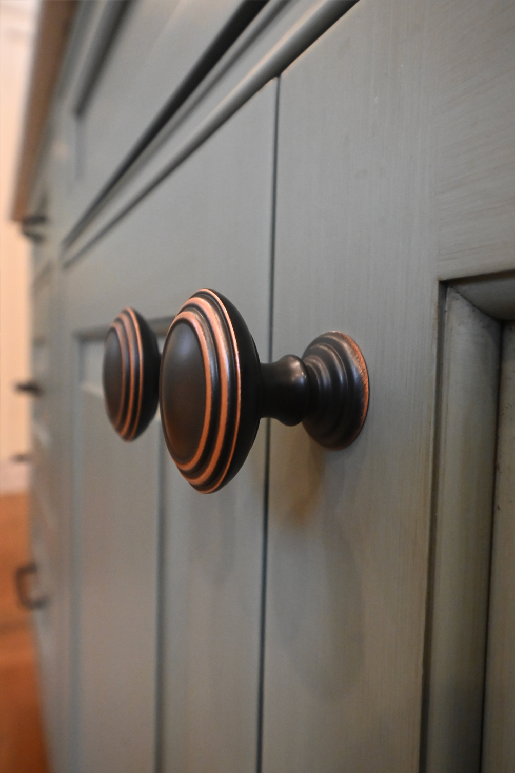 Close-up of a blue cabinet with dark, oval-shaped bronze hardware.