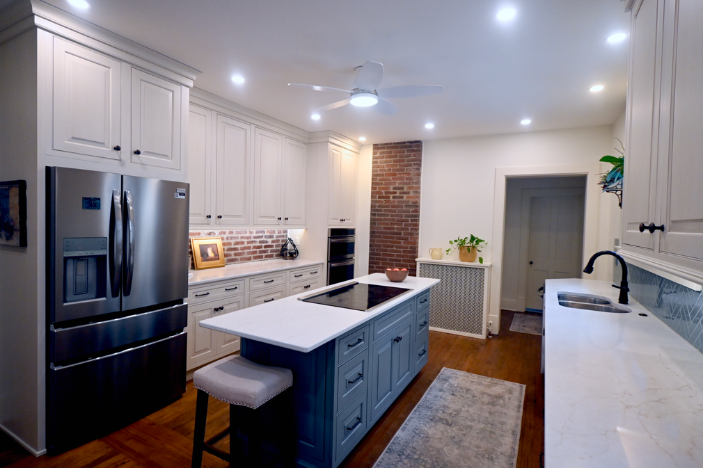 Kitchen with white cabinets, blue island, brick accent wall, and stainless steel refrigerator.