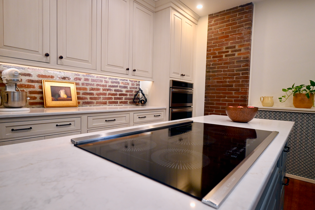 Kitchen with brick backsplash, white cabinets, and island with cooktop.