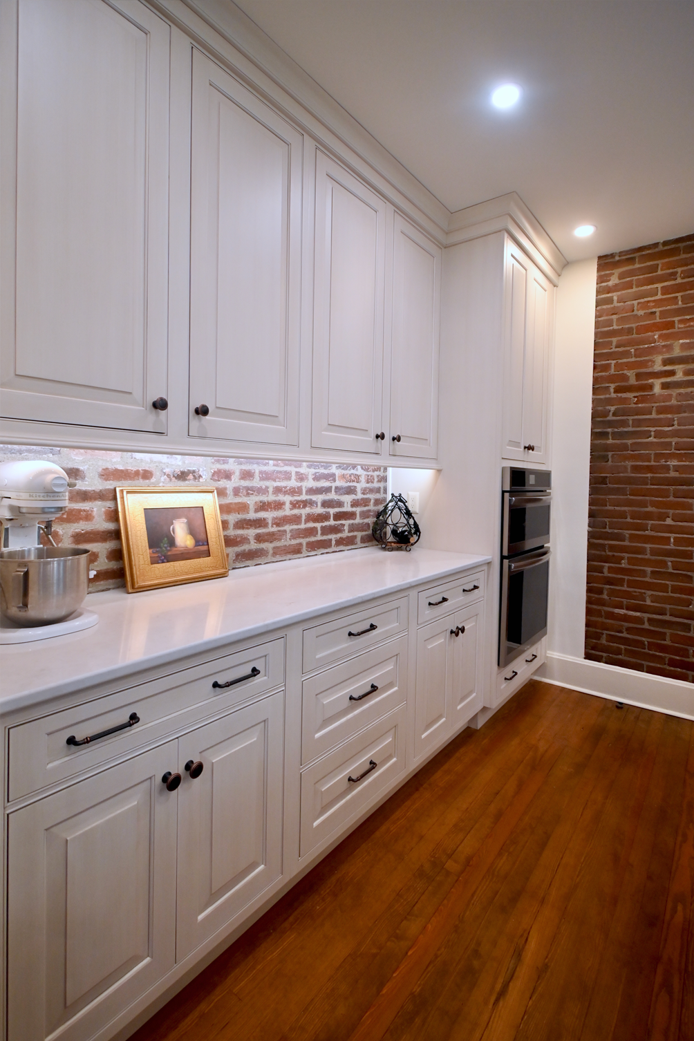 White kitchen cabinets with brick backsplash, wood floor. Built-in oven.
