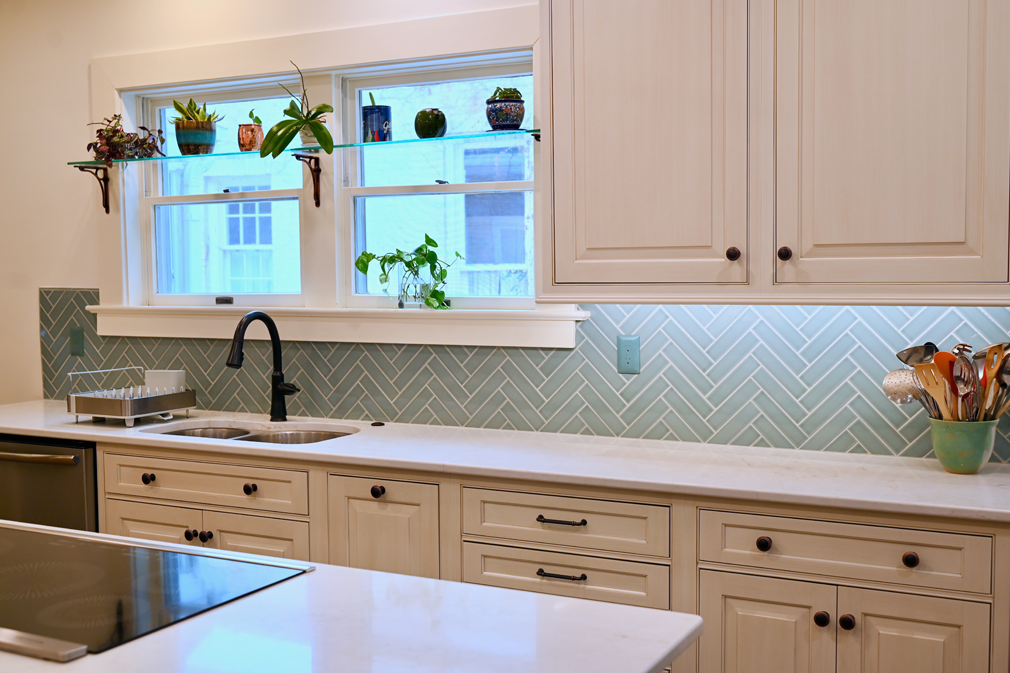 Kitchen with white cabinets, light blue herringbone tile backsplash, and plants in the window.