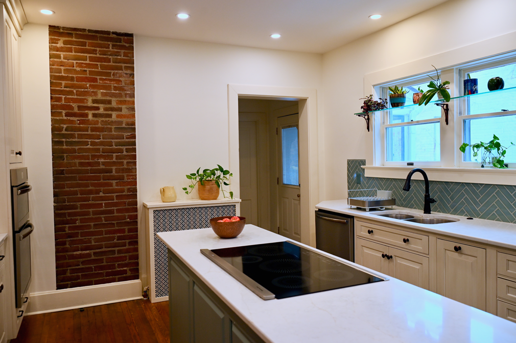 Kitchen with white cabinets, brick wall, and a large island with a stovetop.