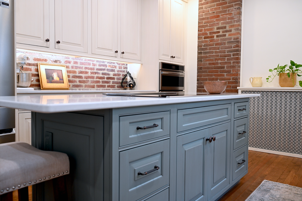 Kitchen with blue island, white cabinets, and exposed brick wall.
