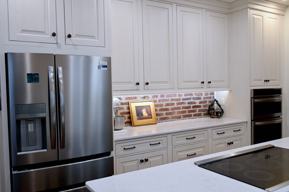 Kitchen with white cabinets, stainless steel refrigerator, brick backsplash, and a cooktop on the island.