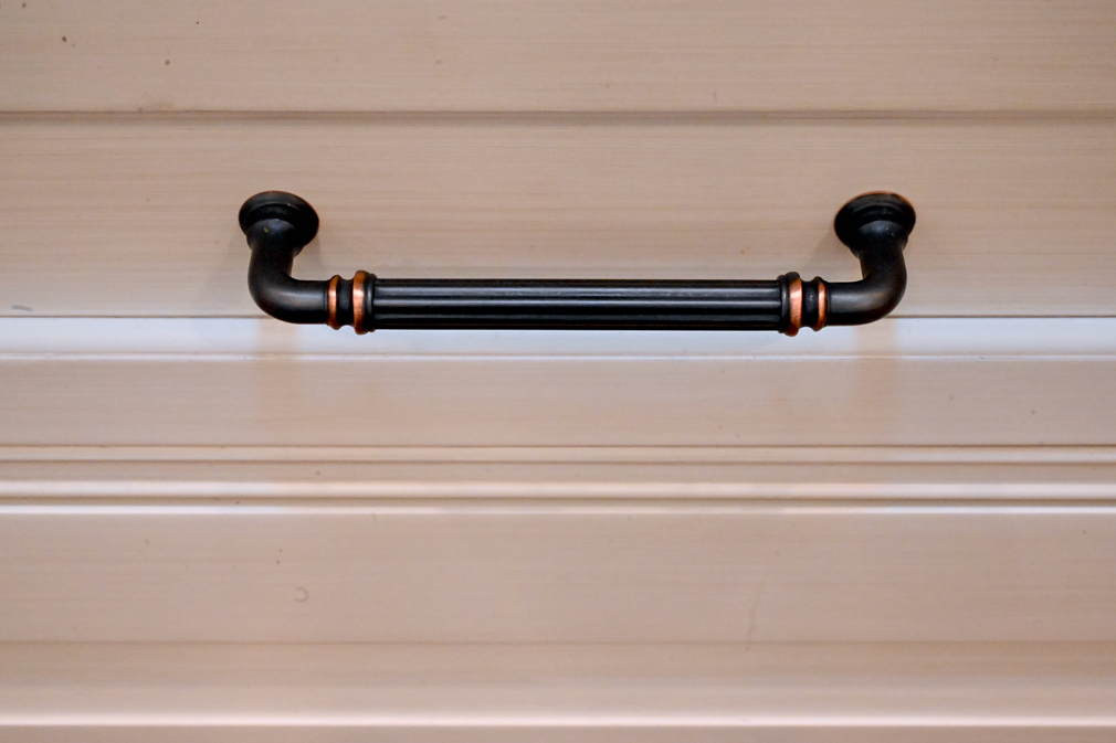 Black and bronze drawer pull on a cream-colored cabinet.