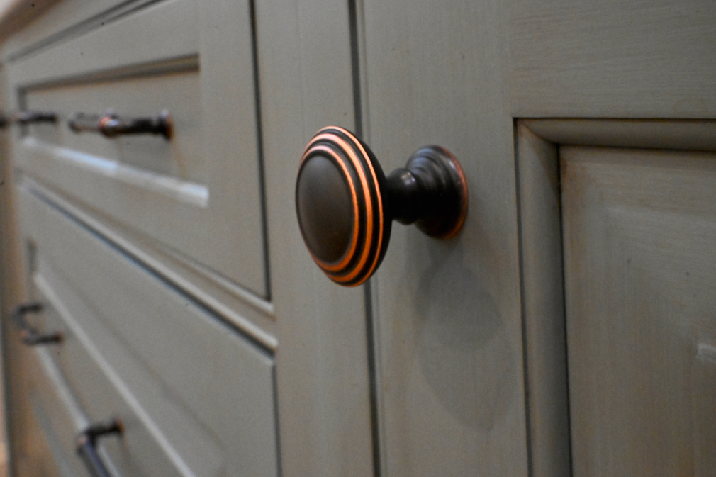 Close-up of a cabinet knob with a copper-tone ring and black finish, on a gray cabinet door.
