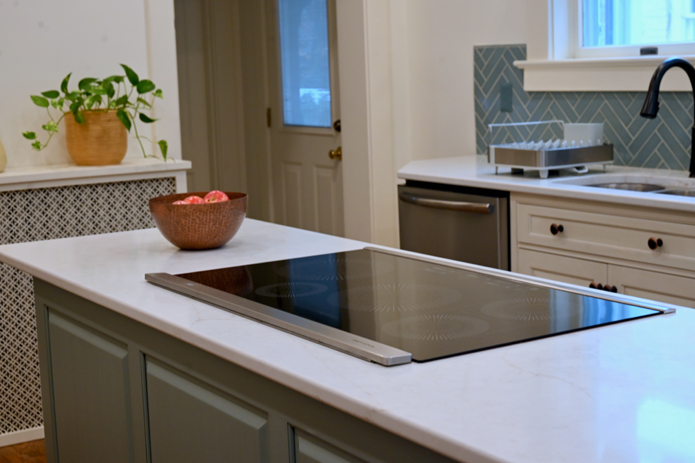 Kitchen island with built-in cooktop, white countertop, and gray cabinets. A copper bowl sits atop.