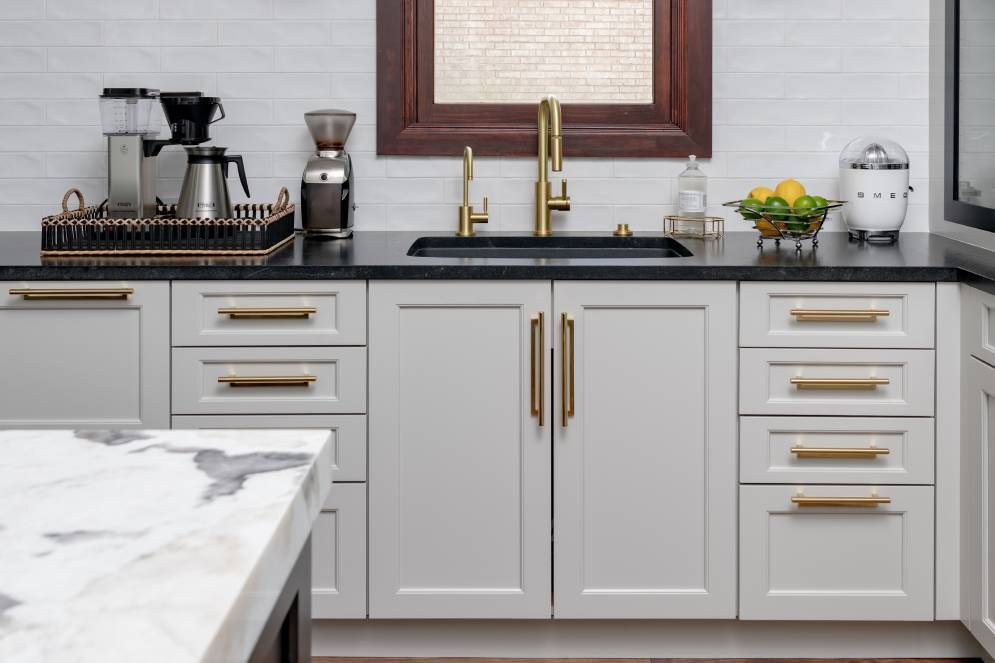 A kitchen with white cabinets , black counter tops , a sink and a window.