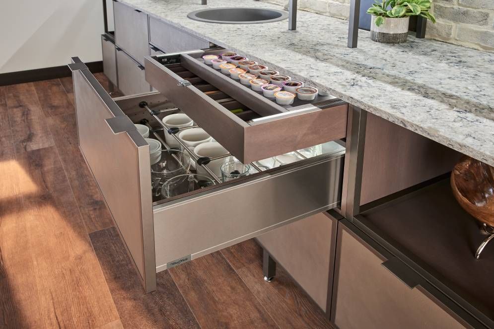 A kitchen with a stainless steel drawer filled with glasses.