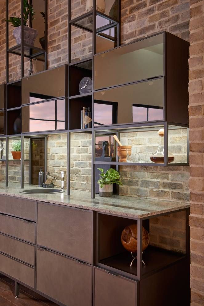 A kitchen with a sink , cabinets , shelves and a brick wall.