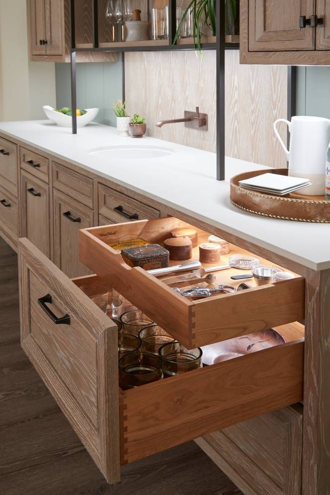 A kitchen with a wooden drawer filled with utensils and glasses.