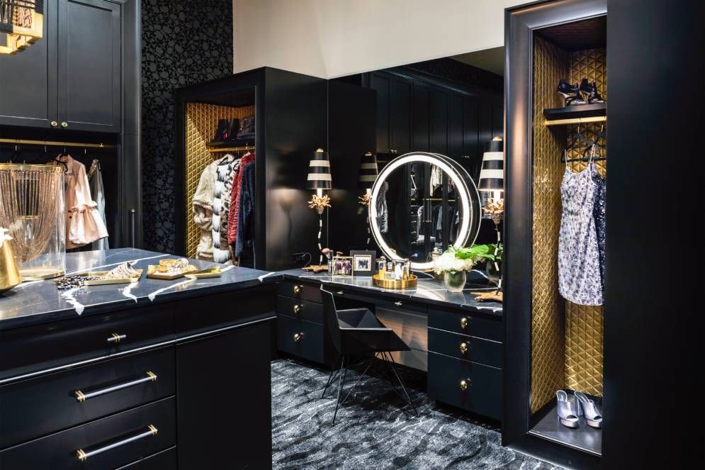 A walk in closet with black cabinets , a vanity , and a mirror.
