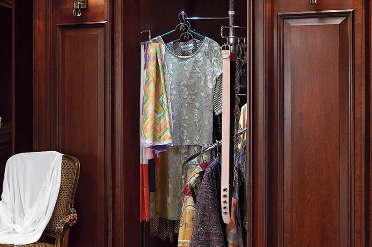 A closet with clothes hanging on racks and a chair.