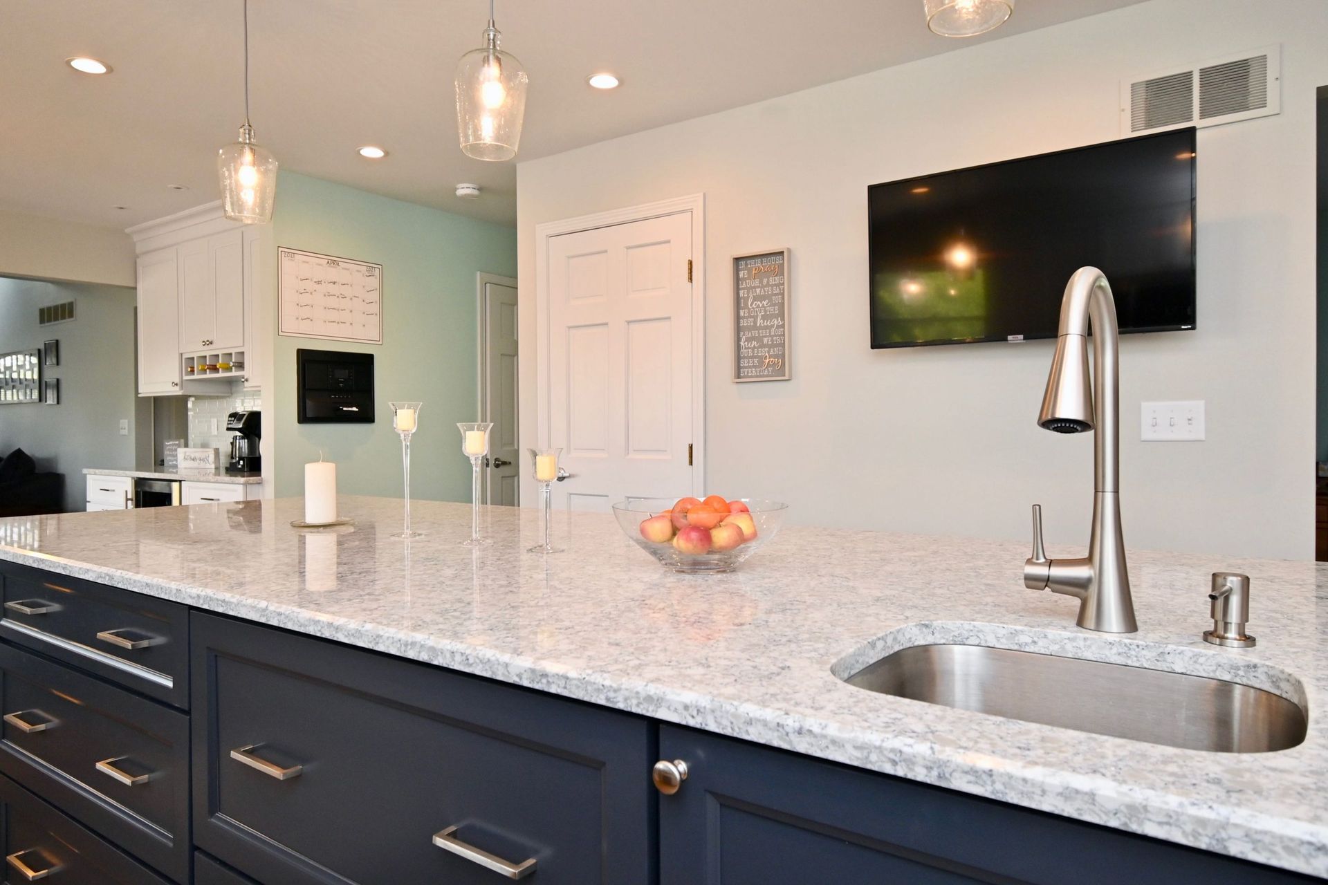 A kitchen with a sink and a television on the wall.
