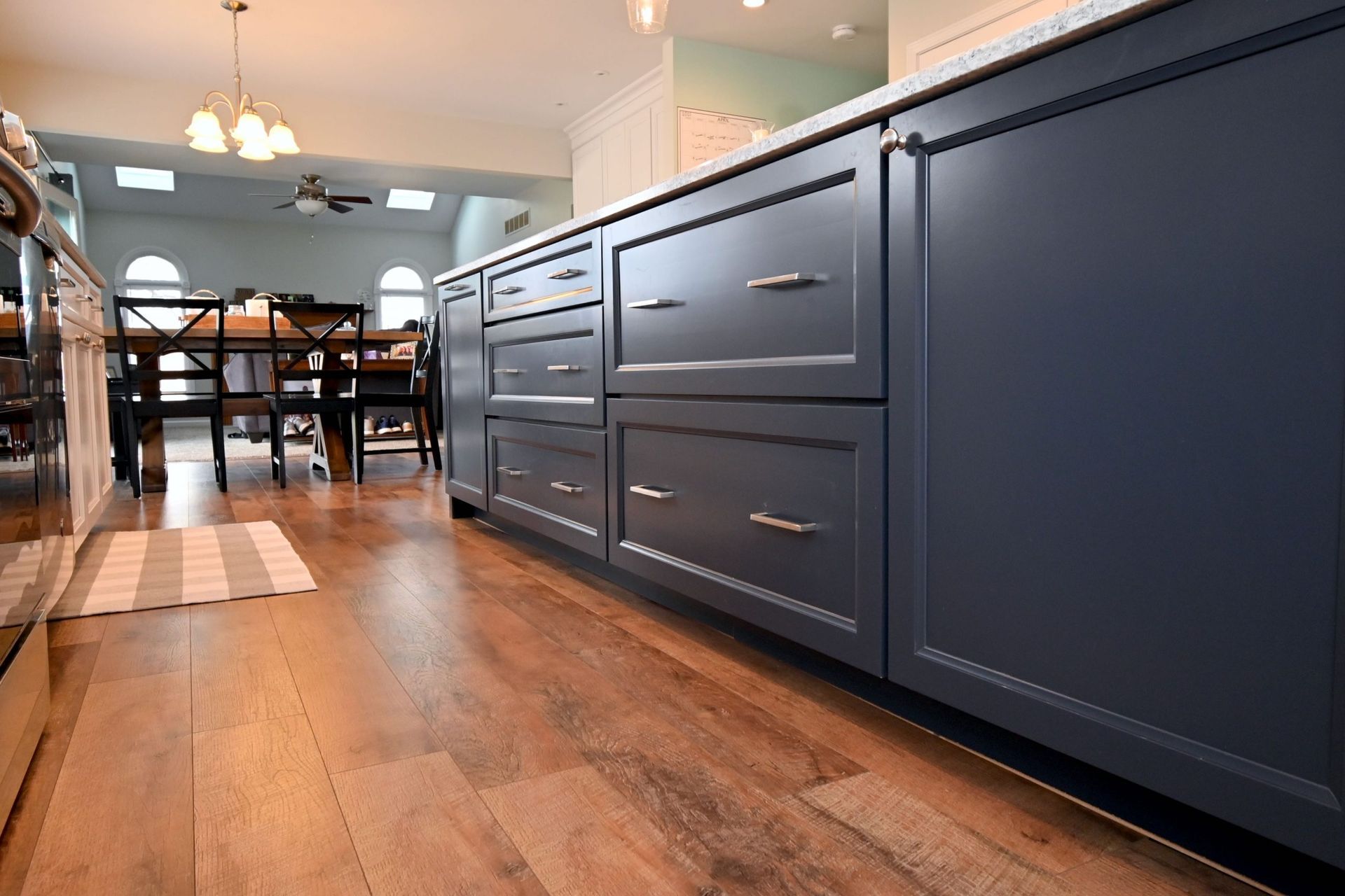 A kitchen with blue cabinets and hardwood floors and a dining room in the background.
