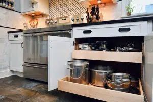 A kitchen with a pull out drawer filled with pots and pans.