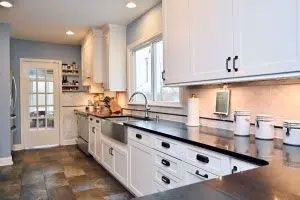 A kitchen with white cabinets , black counter tops , a sink , and a window.