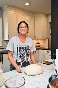 A woman is standing in a kitchen holding a ball of dough.