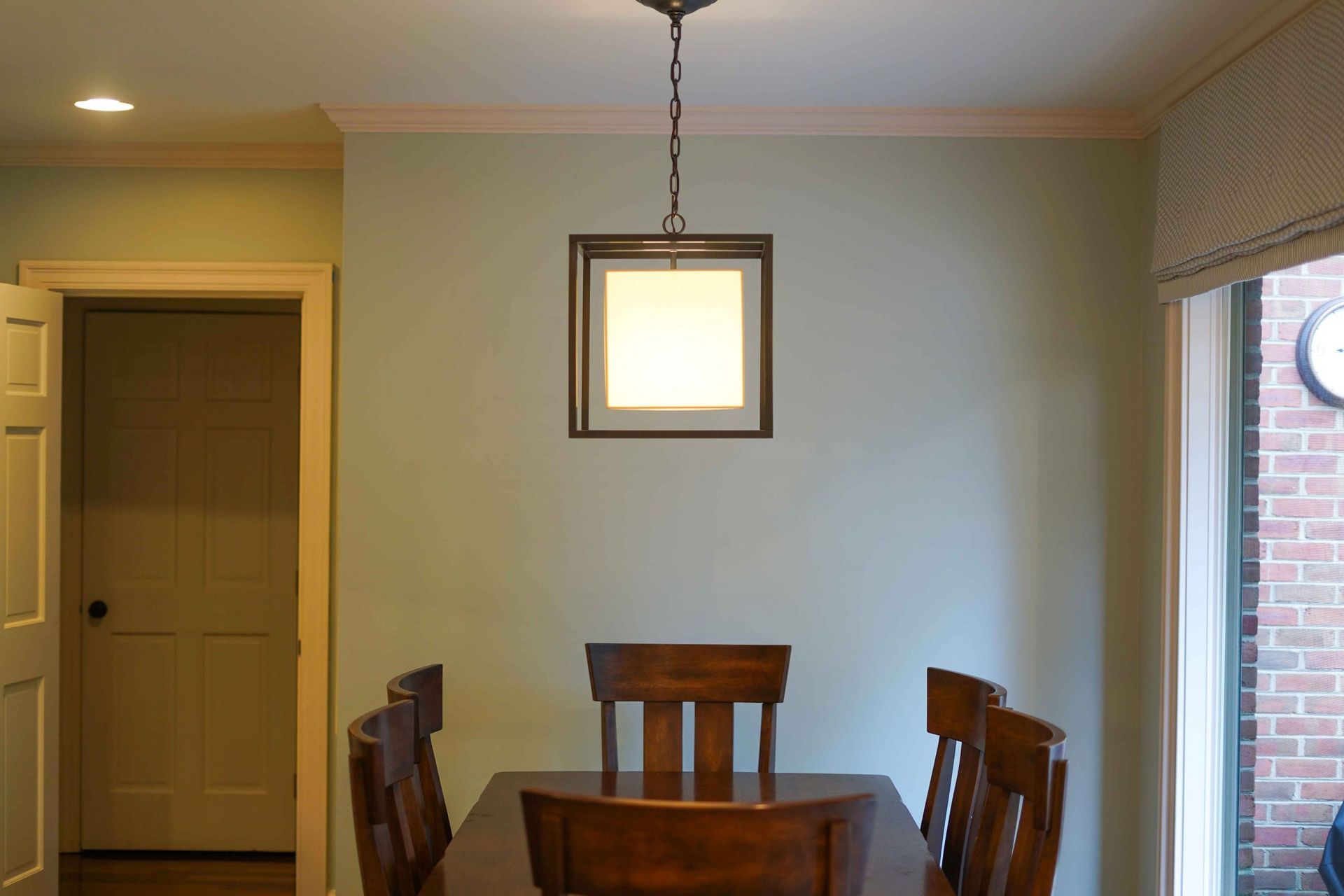 A dining room with a table and chairs and a light hanging from the ceiling.