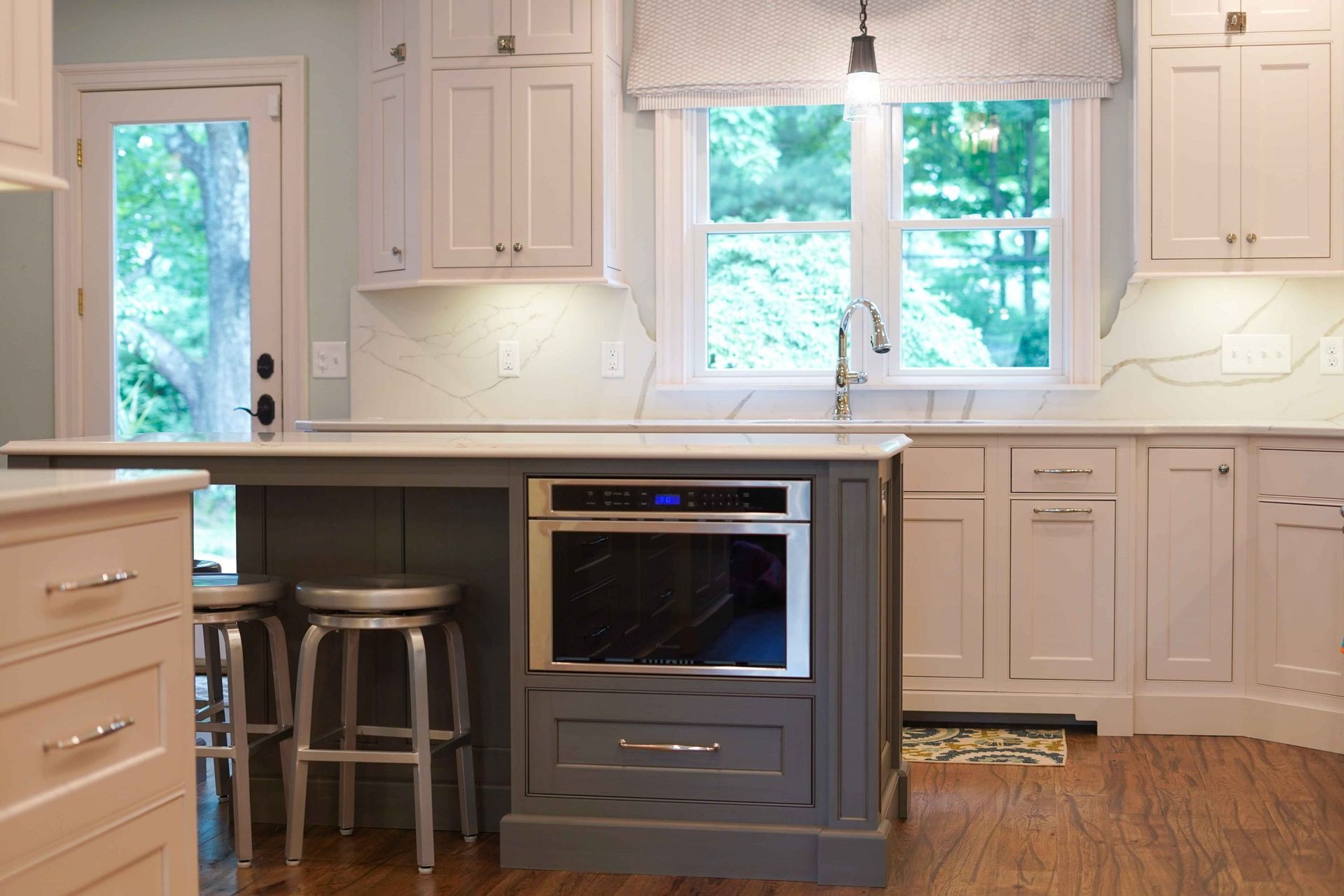 A kitchen with white cabinets and a gray island with a microwave oven.
