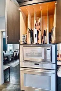 A kitchen with a microwave oven and a cabinet filled with utensils.