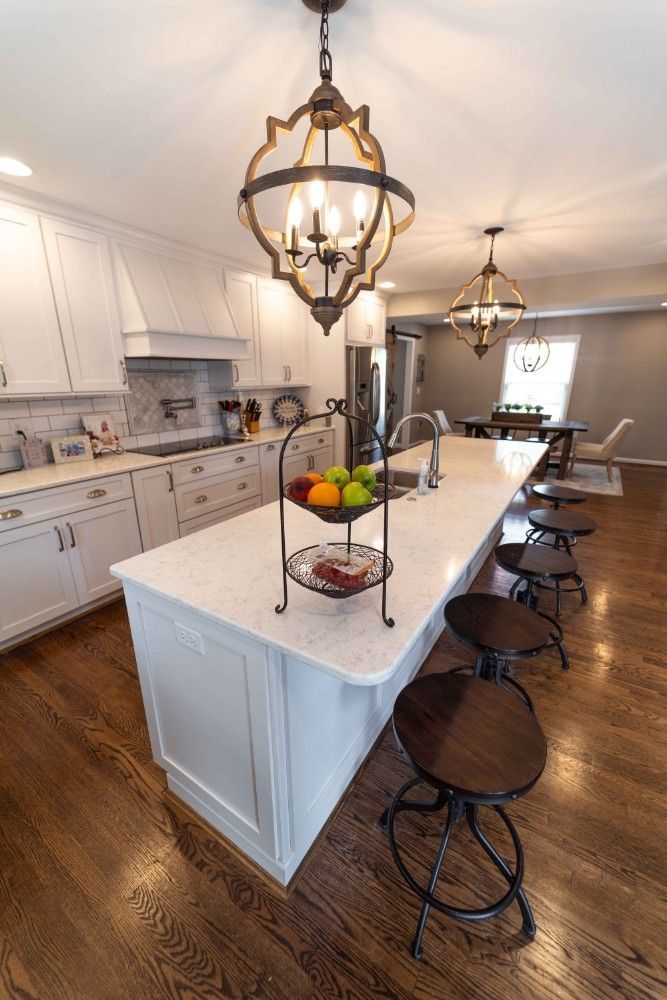 A kitchen with a large island and stools and a chandelier hanging from the ceiling.