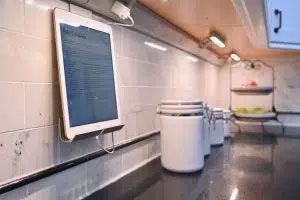 A tablet is hanging on a wall in a kitchen.