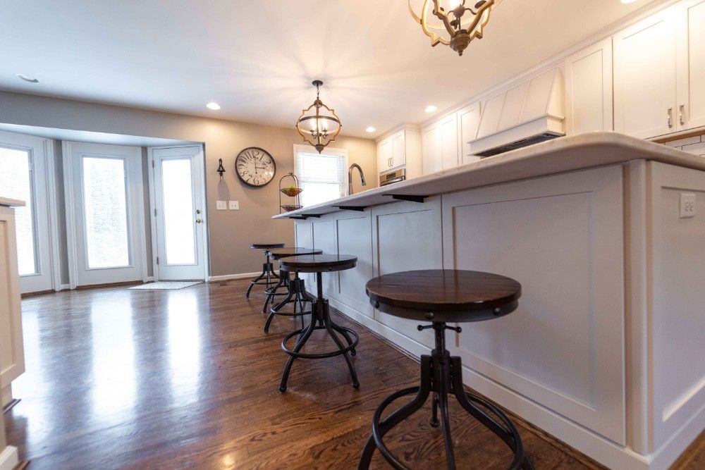 A kitchen with white cabinets and wooden floors and stools.
