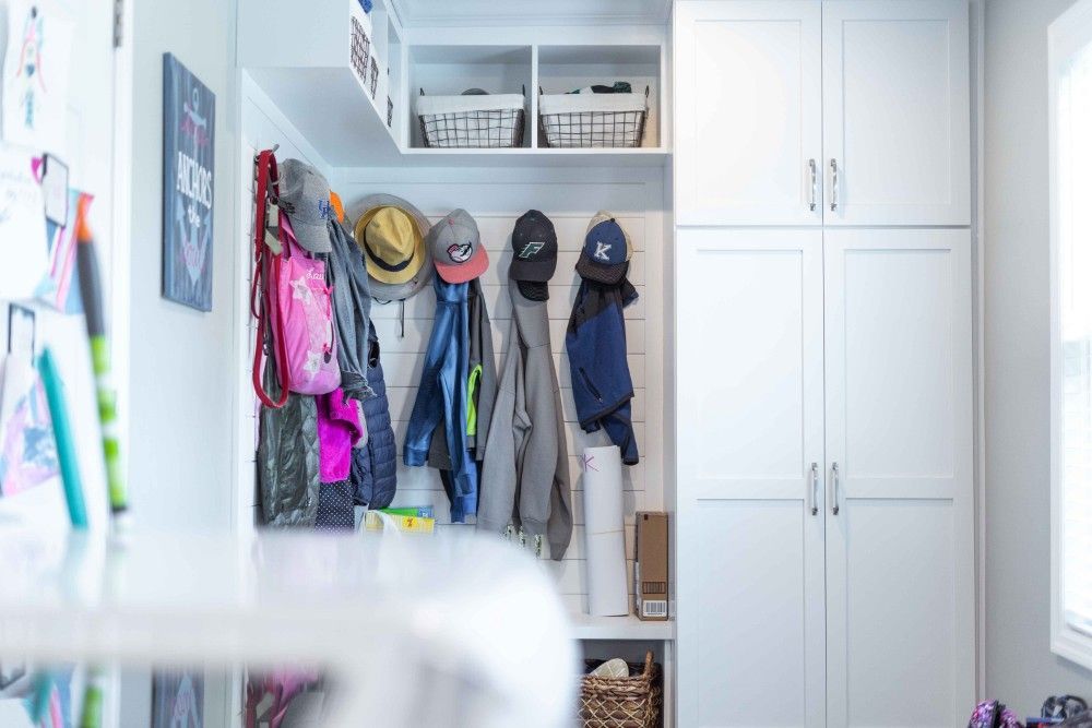 A mud room with white cabinets and hats hanging on the wall.