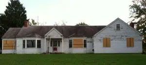 A white house with shutters on the windows is sitting in the middle of a lush green field.