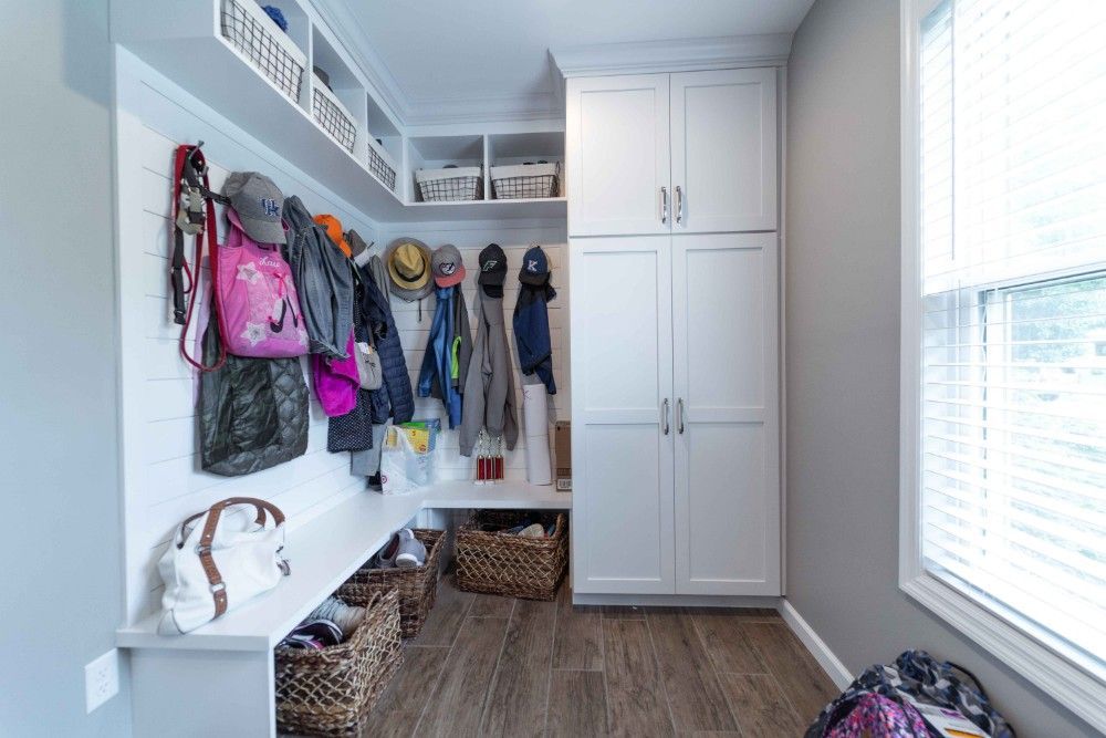 A mud room with white cabinets , a bench , and a window.