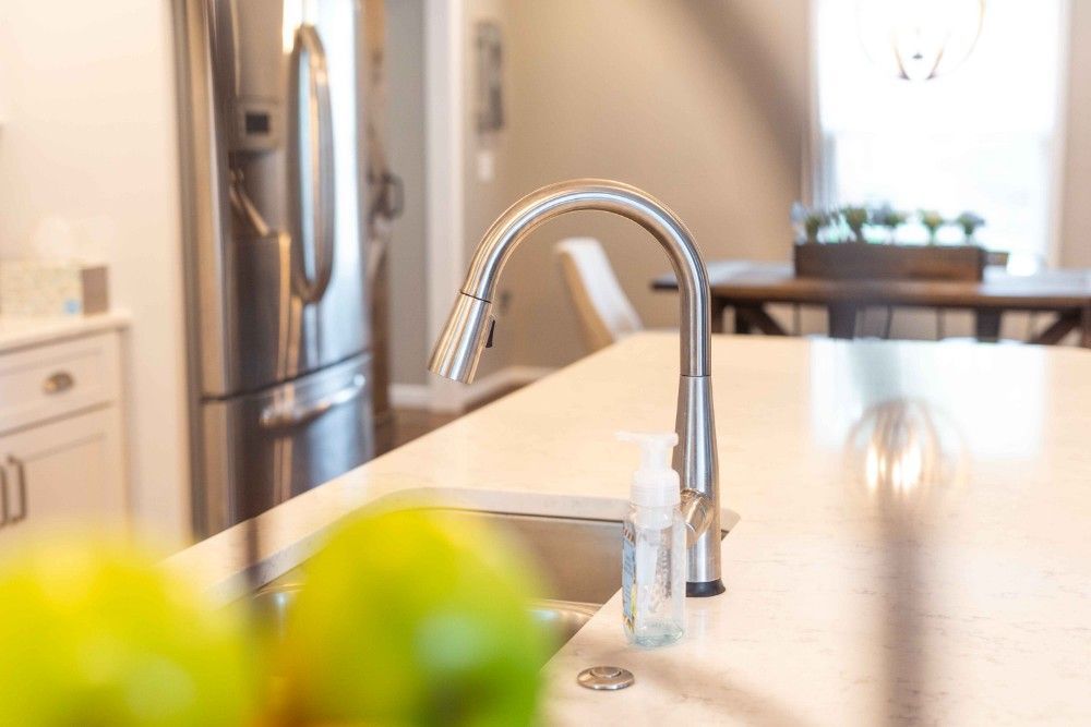 A kitchen sink with a faucet and a refrigerator in the background.