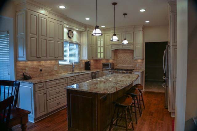 A kitchen with white cabinets , granite counter tops , stools and a large island.