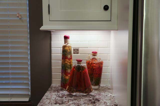Three bottles are sitting on a counter in a kitchen next to a refrigerator.
