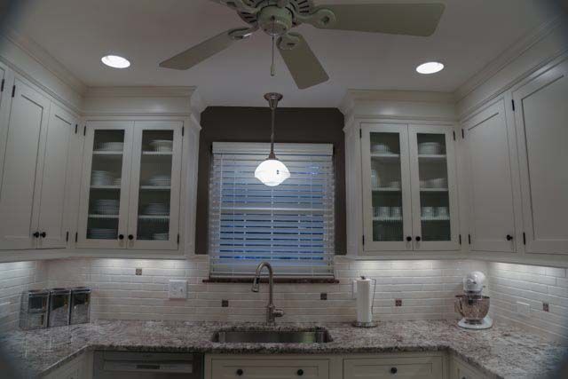 A kitchen with white cabinets , granite counter tops , a sink and a ceiling fan.