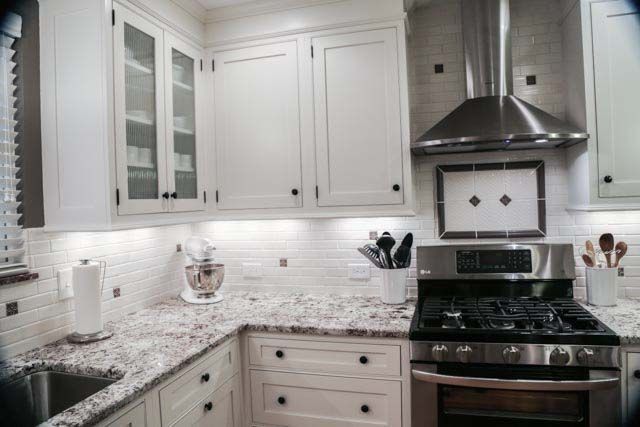 A kitchen with white cabinets , granite counter tops , stainless steel appliances and a stove.