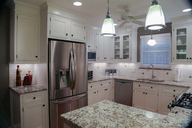A kitchen with white cabinets , granite counter tops , stainless steel appliances and a refrigerator.