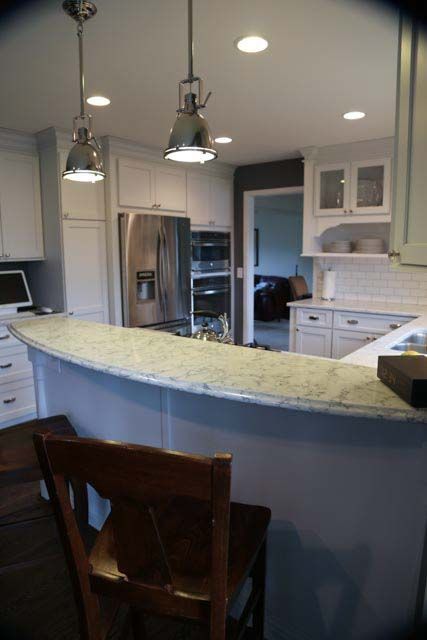 A kitchen with white cabinets , granite counter tops , stainless steel appliances and a bar.