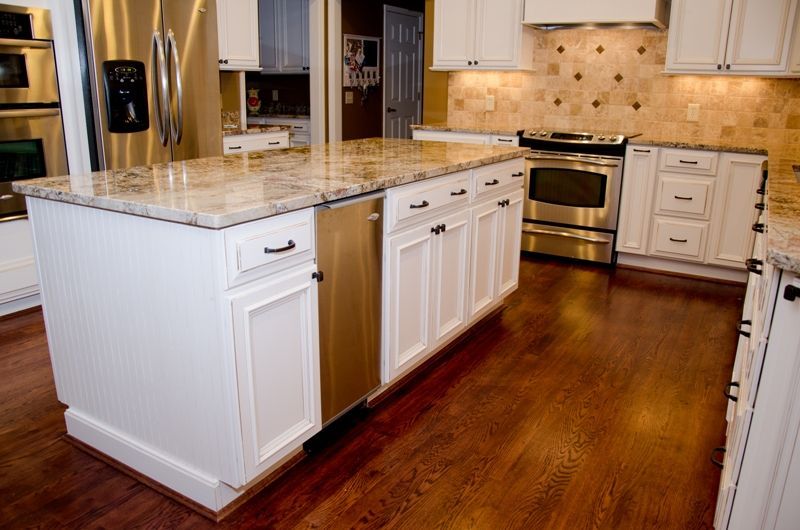A kitchen with white cabinets , granite counter tops , stainless steel appliances and hardwood floors.