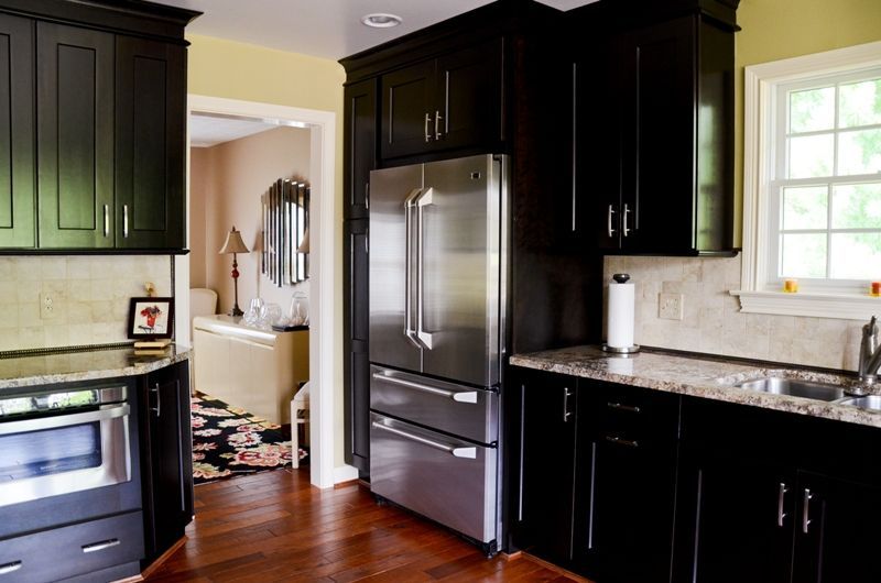 A kitchen with black cabinets and a stainless steel refrigerator