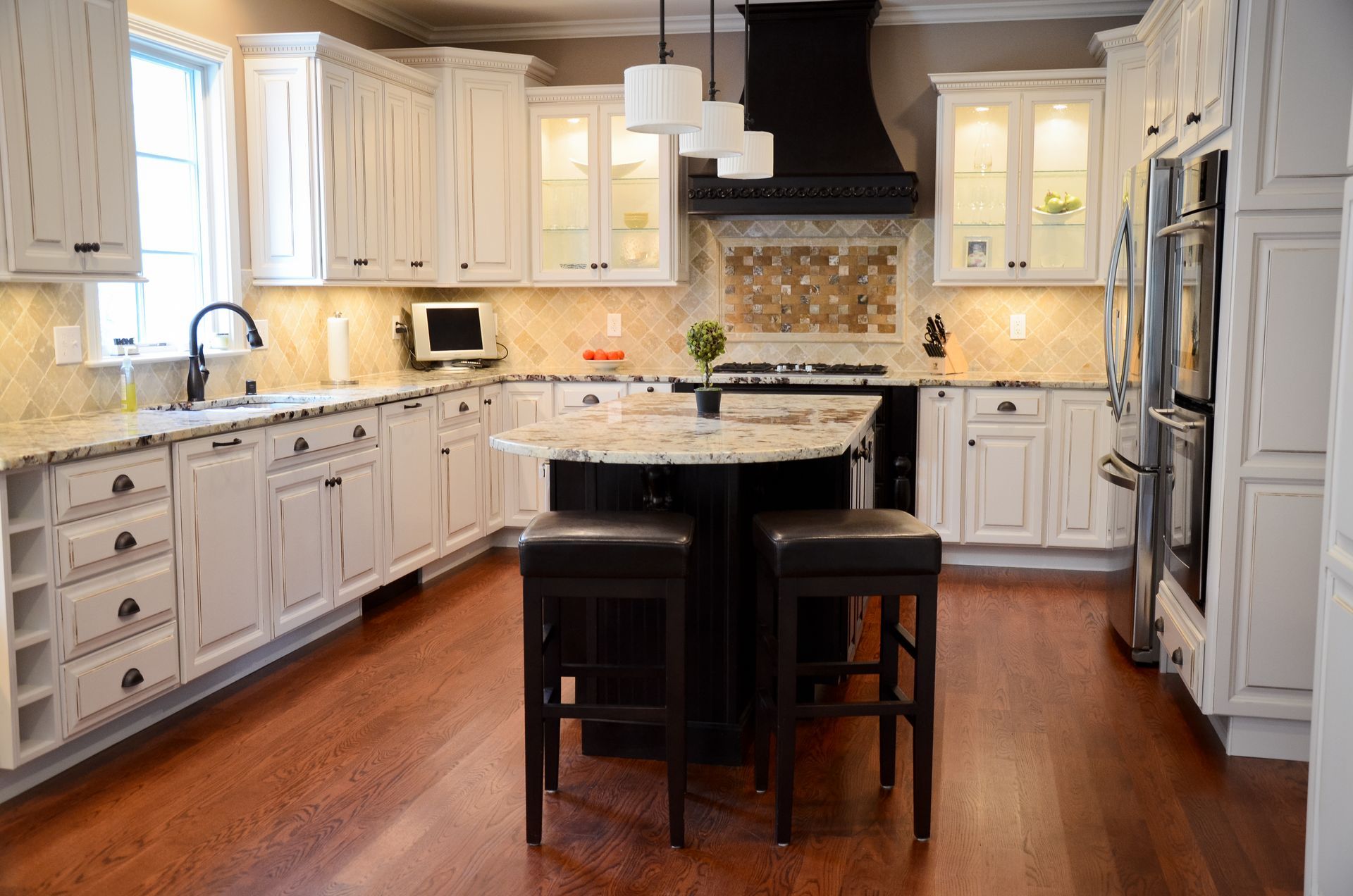 A kitchen with white cabinets , hardwood floors , stainless steel appliances and a large island.