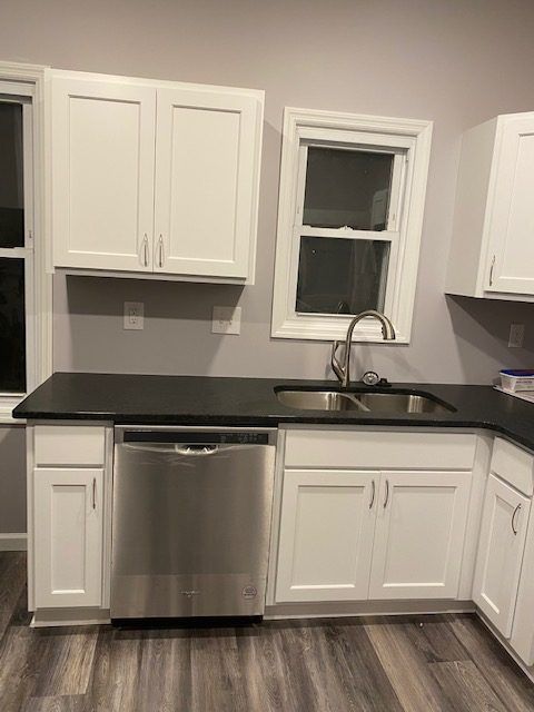A kitchen with white cabinets , a stainless steel dishwasher , a sink , and a window.