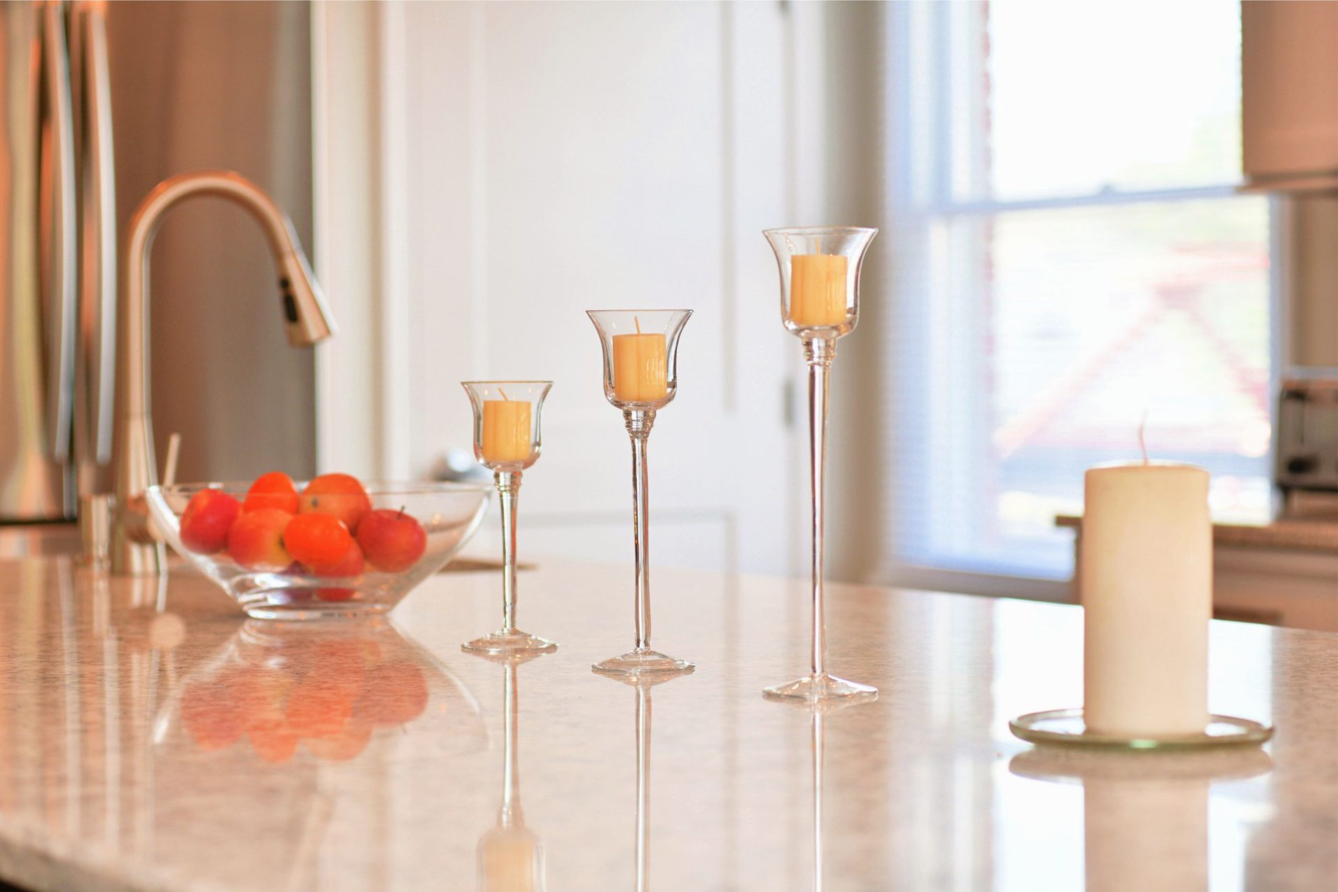 A kitchen counter with three candles and a bowl of fruit.